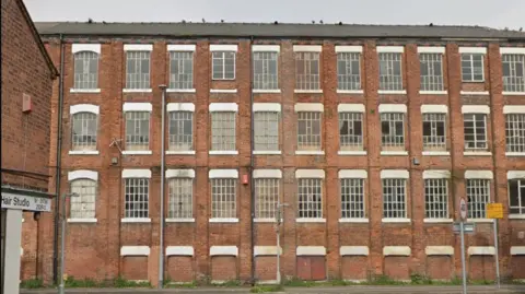 The big, brick building has broken windows on three floors. 
