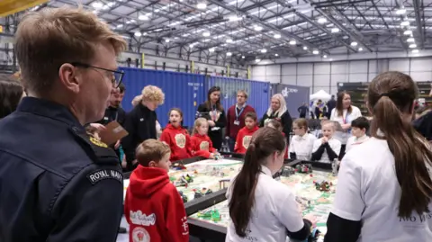 RNAS Culdrose A judge from the Royal Navy watches on as teams of school pupils complete a series of challenges on table with robots they have built out of Lego.