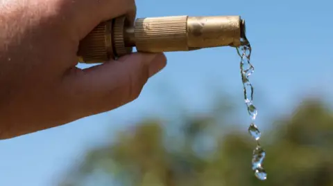 Water dripping from the end of a hosepipe being held up, with a blue sky behind