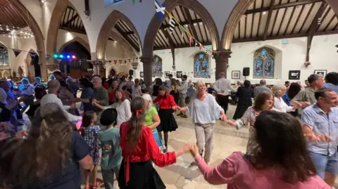 Celtic Gathering People smile as they dance in a circle holding hands