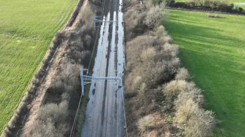 A drone shot of flooded railway tracks with bushes and fields either side.