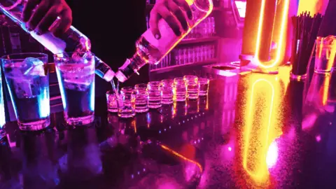 A bartender pours a row of shots from two bottles at the same time.