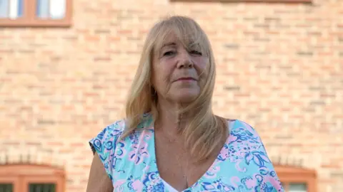A woman with blonde hair while wearing a blue and pink V-neck top
