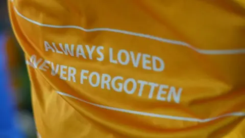 Jamie Niblock/BBC The back of a yellow football jersey that has the slogan: Always Loved, Never Forgotten.