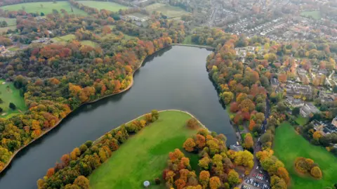 An aerial shot of a large lake surrounded by grass and trees. 