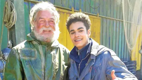 Nick Hayman Nick on the left with a scraggly beard and green coat, next to Will Parry on the right, who is wearing a blue coat, and putting his thumb up at the camera.