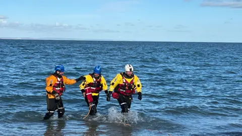 Three coastguards walking out of the water. 