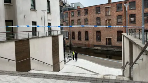 Police near the canal with police tape across a walkway entrance