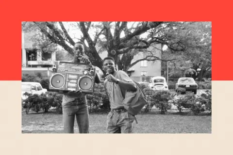 Getty Images Two young men stand by a boombox and smile. The photograph is in black and white