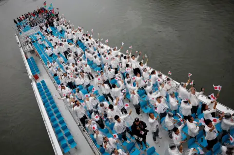  Albert Gea/Reuters Athletes from Japan aboard a boat in the floating parade on the River Seine wave their country's flag