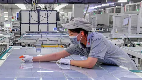 VCG via Getty Images A woman leans over a large sheet of solar panel modules at a factory in Jinhua, Zhejiang Province of China. 