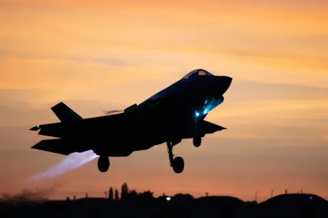 A fighter jet takes off in the shadows off a sunset