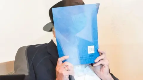AFP Bruno Dey holds a folder in front of his face in court on 23 July 2020