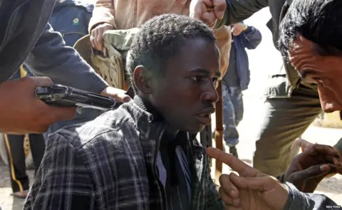 Reuters This photo is from a series taken in Libya in 2011. It shows rebels threatening a man they accuse of being loyalist to then leader Muammer Gaddafi, but is now being shared in connection to the alleged slave trade in the country.