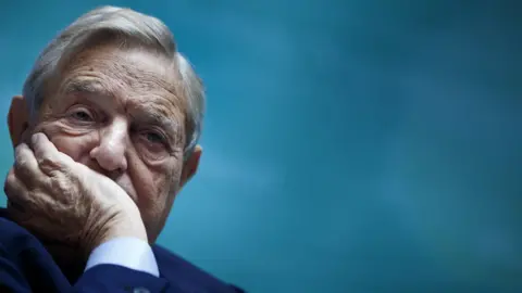 Getty Images George Soros with his hand on his face, pictured in 2011