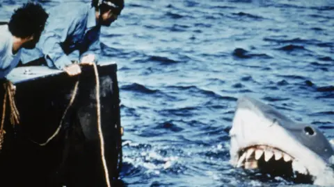 Getty Images Actors Richard Dreyfuss (L) and Robert Shaw lean off the back of their boat, holding ropes as they watch the giant Great White shark emerge from the water in a still from the film, 'Jaws,' directed by Steven Spielberg. (Photo by Universal Pictures/Courtesy of Getty Images)