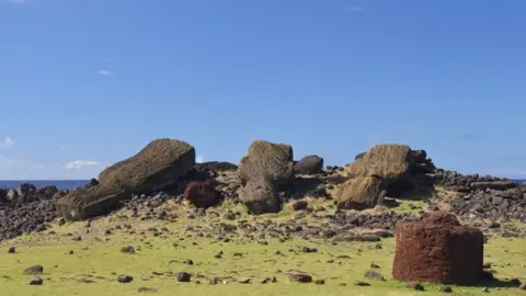 Terry Hunt Red scoria pukao hat with tuff rock in background