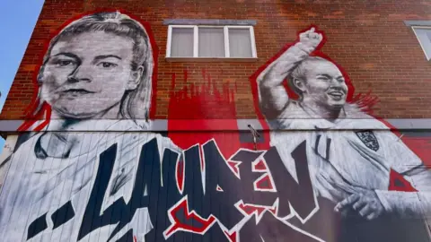 Martin Giles/BBC The large Laurence Hemp mural in North Walsham features two images of the England star, on the left she looks ahead, while to the right she raises her right arm after scoring