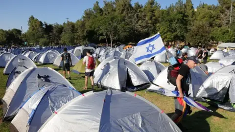 ABIR SULTAN/EPA-EFE/REX/Shutterstock Anti-government protesters stand among tents after spending the night in a tent camp at Sacher Park, near the Israeli Knesset, following a four-day protest march to Jerusalem against the government's planned justice system reform, in Jerusalem, 23 July 2023.