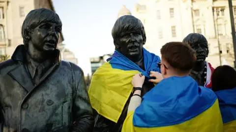 PA Media Man putting an Ukrainian flag on the Beatles Statue at Pier Head in Liverpoo