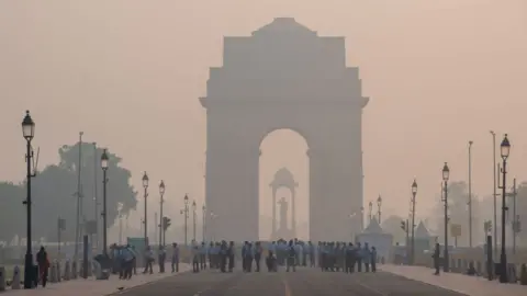 Getty Images NEW DELHI, INDIA - 2023/11/01: India Gate with visitors seen shrouded in smog during the early morning. Air pollution in Delhi is primarily due to vehicles, industries, construction dust, waste burning, and crop residue burning. In winter, temperature inversions worsen the problem by trapping pollutants near the ground. (Photo by Pradeep Gaur/SOPA Images/LightRocket via Getty Images)