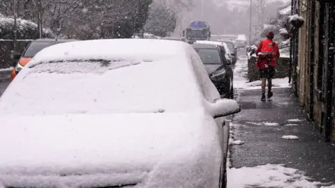 PA Media A postal delivery worker wearing shorts in heavy snow fall during his delivery rounds in Oldham, Greater Manchester