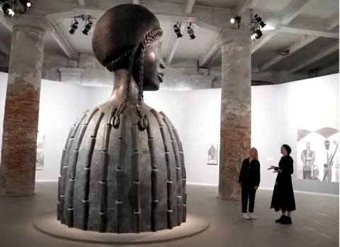 Jack Garland Cecilia Alemani and BBC correspondent Katie Razzall observing Brick House by Simone Leigh