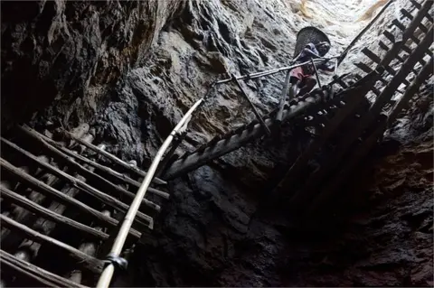 Getty Images In this photograph taken on January 31, 2013, a miner slowly carries a heavy load of wet coal on a basket hundreds of feet up on wooden slats that brace the sides of a deep coal mine shaft near Rimbay village in the Indian northeastern state of Meghalaya. Thousands of private mines employ slim men and boys that will fit in thin holes branching out from deep shafts dug out from the ground in the East Jaintia Hills in Northeastern Indian state of Meghalaya