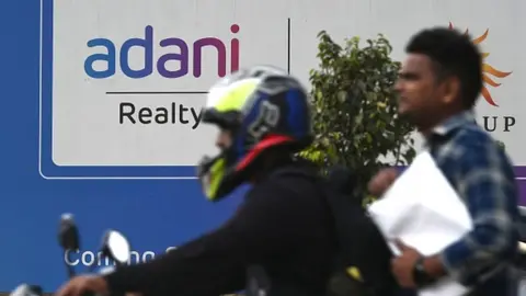 Getty Images Motorists ride past a signage of an upcoming residential project by Adani Realty, a company under Adani Group