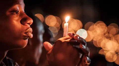 A person holds a candle during a night vigil and prayer at the Amahoro Stadium in Kigali