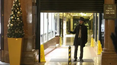 PA Media A doorman watches as the shutters come down at the Argyll Arcade in Glasgow as the new restrictions come into place