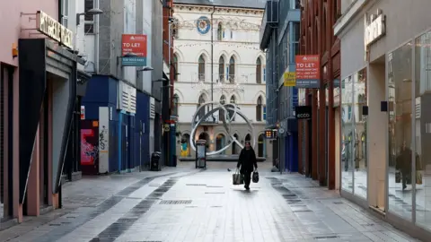 Reuters A woman walks along a deserted shopping street in Belfast city centre