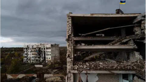 Getty Images A Ukrainian flag flies over a ruined apartment block in he recaptured village of Archangelske, in Kherson province