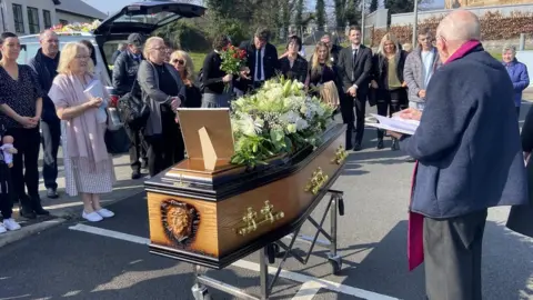 Pacemaker Fr John Craven with mourners in the carpark of Holy Cross Church after it was disrupted by a security alert