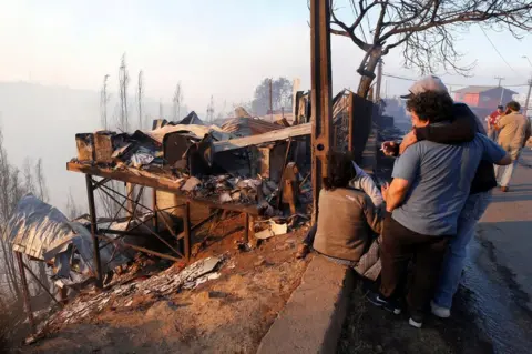 Reuters People react next to the debris of their house following the spread of wildfires in Valparaiso, Chile, 24 December 2019