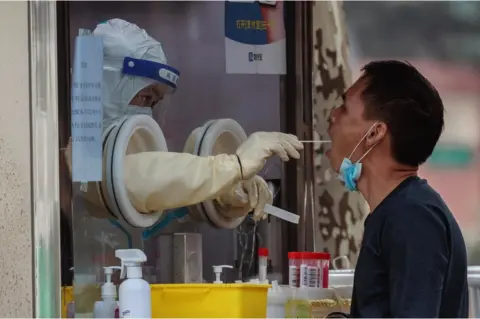 Alex Plavevski / EPA-EFE A man undergoes a coronavirus PCR test at a makeshift testing booth in Shanghai