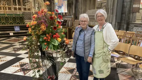 David Webster/BBC Judy Wynn and Mary Foister stood next to red and orange flower exhibition