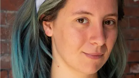 Nia Crockford Nia Crockford. Nia is a 26-year-old white woman with shoulder length hair that she has dyed blue. She wears a pale blue headband to keep it back from her face. She has brown eyes and smiles at the camera. She is pictured outside against a brick wall