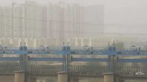 Getty Images Vehicles cross a barrage on Hindon river as dust covers the skyline on the outskirts of New Delhi