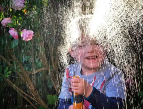 Nick Morton A boy playing with water from a hose-pipe