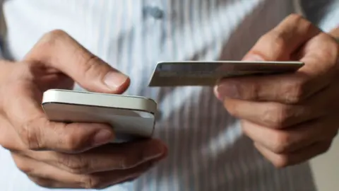 Getty Images Person holding phone and bank card