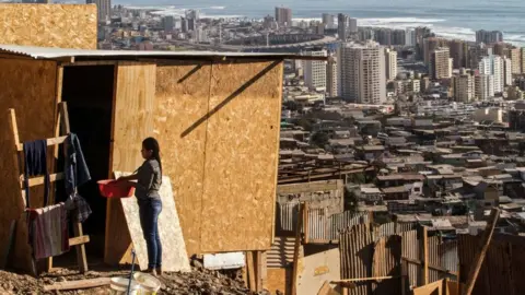 Glenn Arcos/AFP A woman stands outside her house at a camp in Altamira, Antofagasta, Chile, with the city of Antofagasta in the background, on 27 April