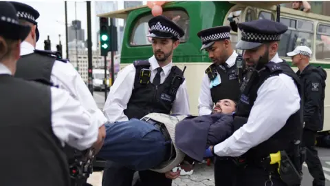 PA Media Police remove a demonstrator from a bus parked on London Bridge