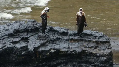Getty Images Repsol employees wearing biosafety suits work on the oil spill cleanup at the shore of Cavero Beach