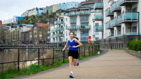 Bristol University Ella runs by the harbour with Bristol's colourful houses behind her