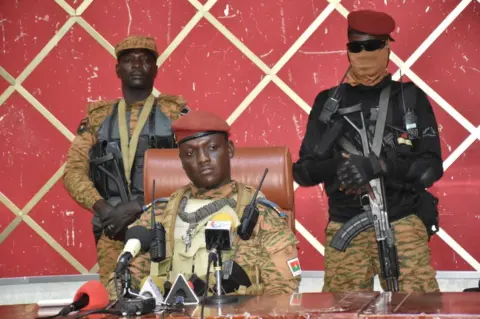 Getty Images Capt Ibrahim Traoré flanked by soldiers as he addresses politicians.