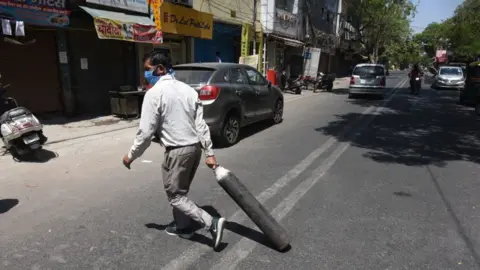 Getty Images A family member of Covid-19 patient carries an empty cylinder to refill outside the oxygen filling centre at Dilshad Garden Area on April 25, 2021 in New Delhi, India.