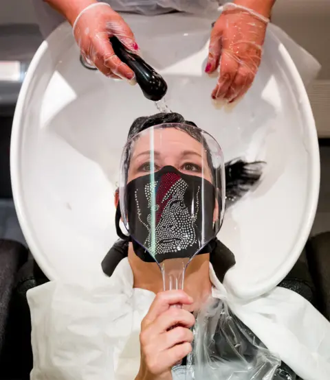 Getty Images A customer wearing a face mask with David Bowie's face on has her hair washed in a hair salon