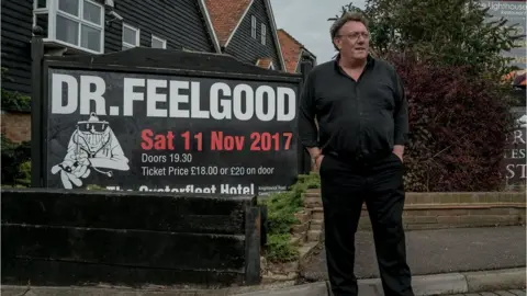 BBC Chris Fenwick beside a Dr Feelgood poster