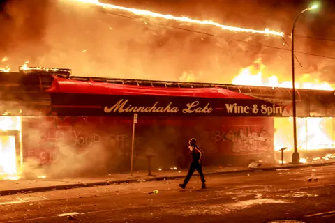 Getty Images A man walks past a liquor store in flames